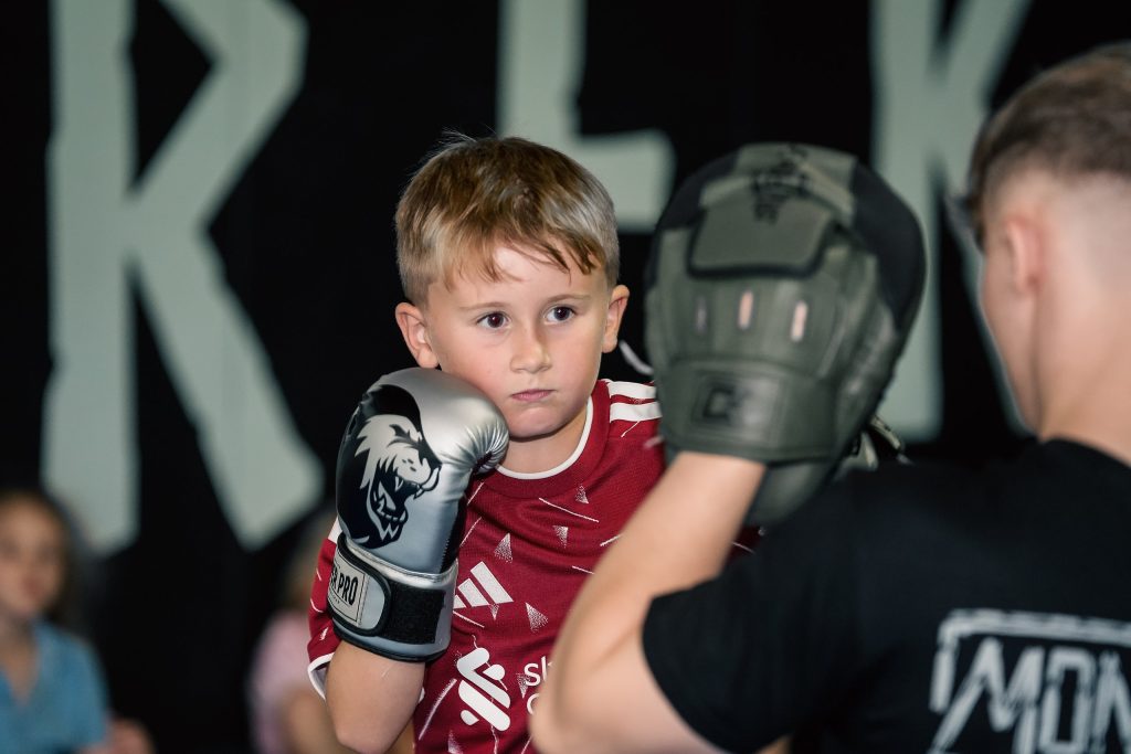 Young boy in boxing gloves hitting pads with a coach during an SBG Kids class